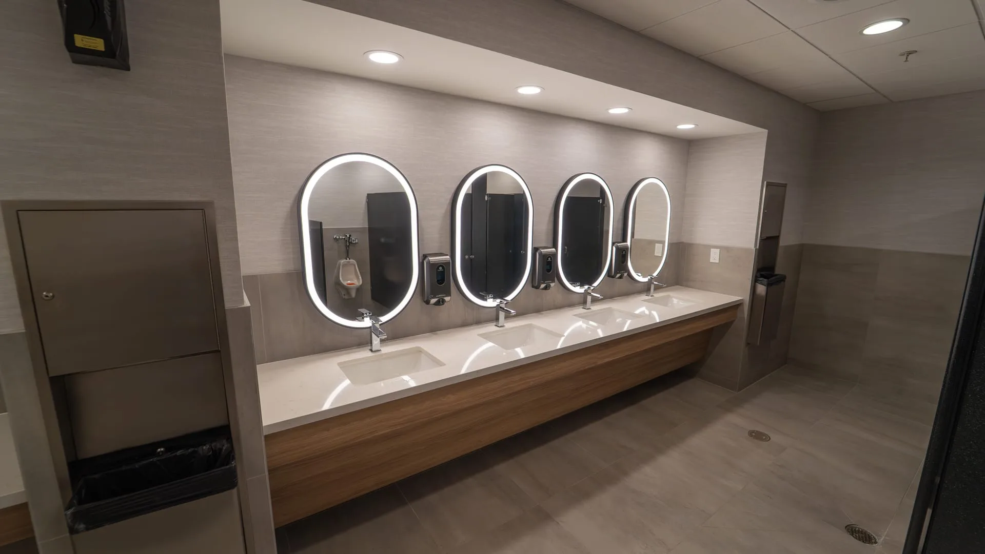 Restroom vanity with four sinks, a light countertop, wood-look front and illuminated oval mirrors